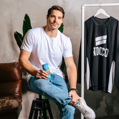 Athlete seated with a can of NOCCO BCAA, a NOCCO jersey hanging on a rail behind him