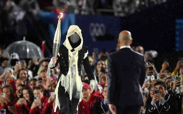 The masked torchbearer of the Paris 2024 Olympic opening ceremony carrying the flame through the crowd
